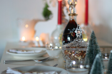 Table set for Christmas meal, with plates, wine, decorations and lit candles. Selective focus.