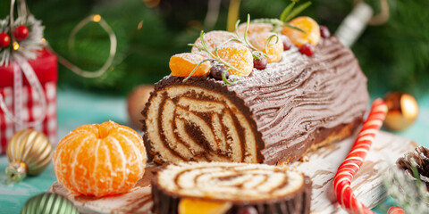 Yule log roll cake with chocolate ganache on Christmas decorated background