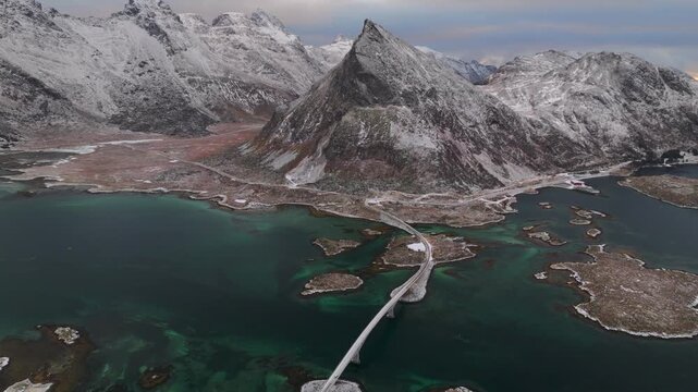 Aerial view of Fredvang Bridges cutting through the turquoise waters, with snow-dusted mountains as a majestic backdrop, Fredvang, Nordland, Norway.