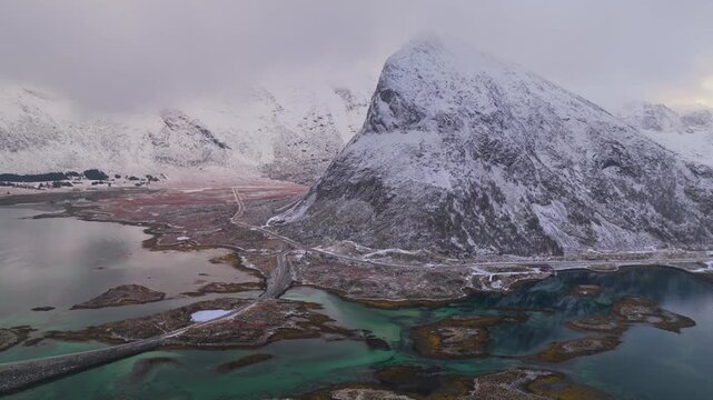 Aerial view of snowy mountains and bridges contrasting with the turquoise waters, creating a stunning landscape, Fredvang, Nordland, Norway.
