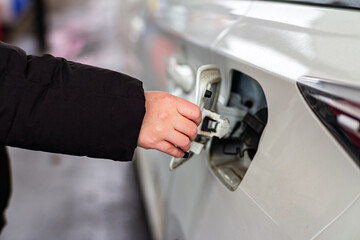 Close up of a person opening the fuel cap of a white car, showing the hand