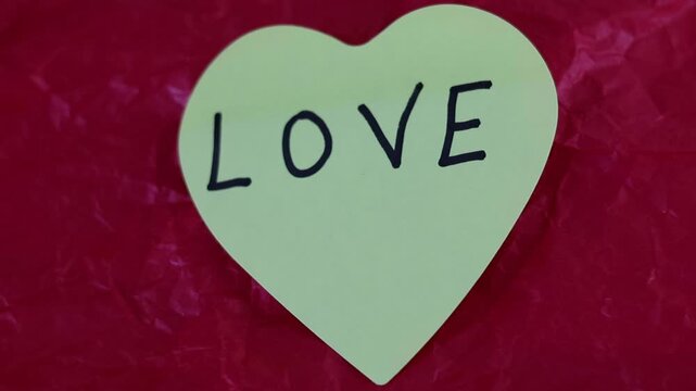 Un primer plano de una nota con forma de coraz&oacute;n con la palabra amor en un fondo rojo