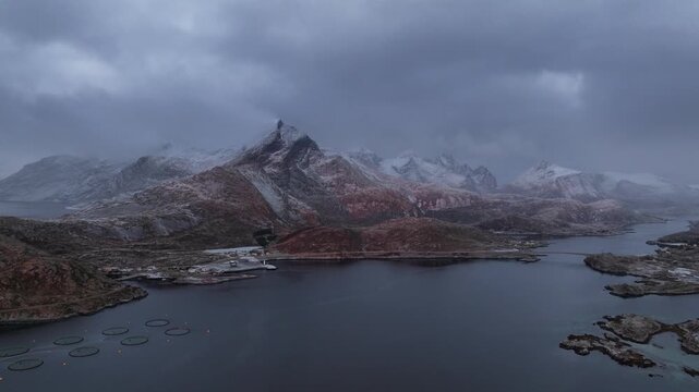 Aerial view of the Ballstad area, showing the contrast between the snow-covered mountains and the dark water surrounded by the rocky land, Ballstad, Nordland, Norway.