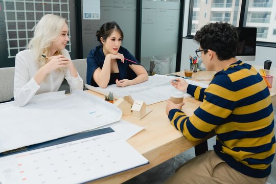 Three diverse professionals are deeply engaged in consultation, reviewing technical blueprints and small architectural models. discuss project planning, design strategy, future real estate development