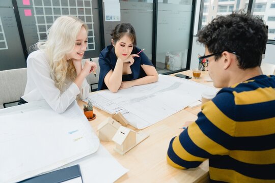 Three diverse colleagues are focus and engaged, reviewing technical blueprints and architectural models on office. team discusses strategic project planning, design execution, attention detail during