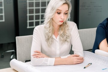 Focused professional woman concentrating on complex technical blueprints during strategic design review and critical problem solving
