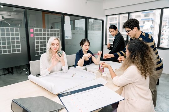 Diverse project management team collaborating on architectural blueprints, calendar schedule, and digital data in a strategic meeting