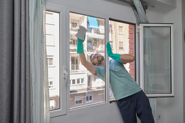 Man cleaning windows at home. Person wearing rubber gloves washing glass with sponge and spray. Couple doing household chores together. Concept of home cleaning, hygiene, and domestic life