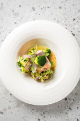 Close-up of a gourmet plated dish featuring pan-seared salmon fillet, broccoli florets, romanesco, fresh sprouts, and clams in a savory broth served in a white bowl.