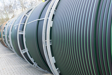 Large industrial pipe coils with green-striped tubing neatly wound on metal reels, stored outdoors...
