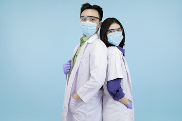 Confident Asian medical professionals in lab coats and safety gear, standing back-to-back, symbolizing strong teamwork and healthcare in blue studio background