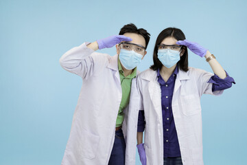 Asian medical professionals saluting or shielding eyes, symbolizing vigilance, foresight, and searching for a solution or threat in blue studio background
