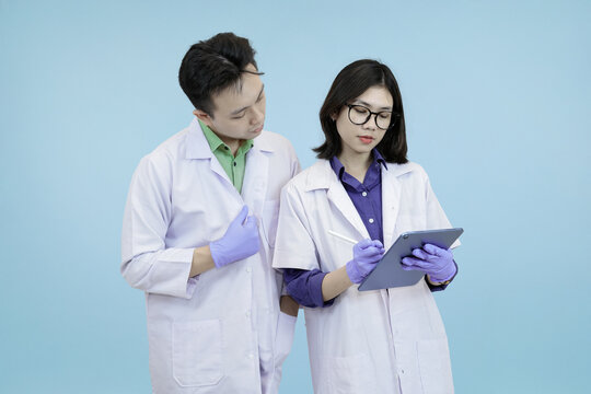 Pensive Asian science professionals closely examining data on a digital tablet, symbolizing focused analysis and problem-solving during research in studio blue background