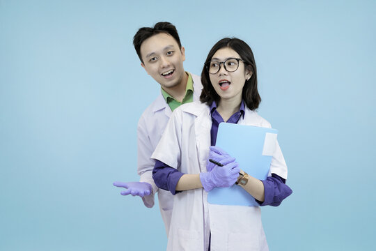 Astonished Asian science professionals reacting to a breakthrough, excitedly viewing data on a digital tablet during research in blue studio background