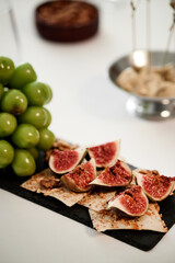 Closeup showing sliced figs arranged on crispbread with green grapes on side, gourmet appetizer prepared for wine tasting event, no people visible in frame