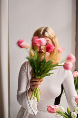 Elegant blonde woman gazing amidst tulip arrangement in studio