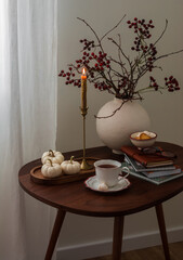 A cup of tea, a vase with cranberry branches, autumn decor, a candle on a wooden table in the living room
