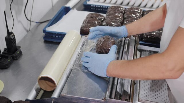 A worker is packaging black bread rolls in a factory. Bakery production
