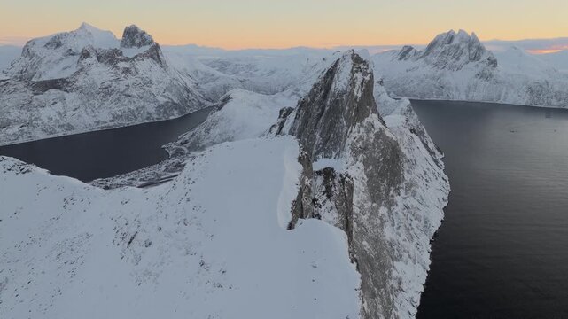 Aerial view of the snow-covered Segla mountain peak, contrasting with the dark blue waters, creating a stunning landscape, Senjahopen, Troms, Norway.