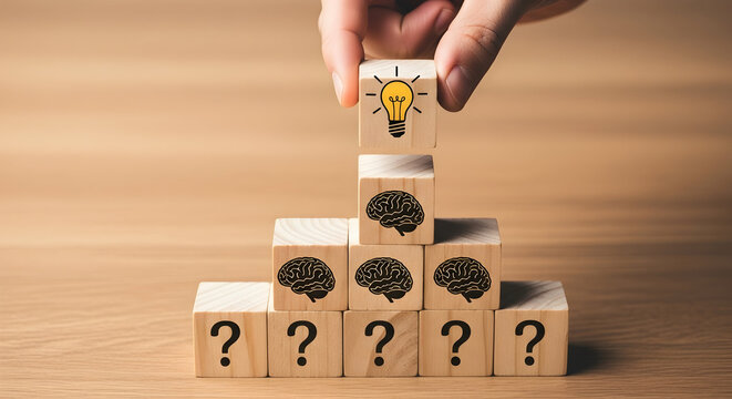Hand places lightbulb block atop brain and question mark blocks symbolizing idea generation and problem solving on a wooden surface representing business strategy and innovation