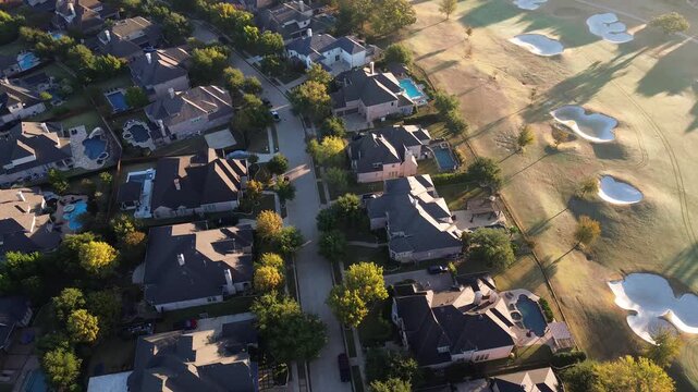 Lantana Golf Club fairway bordered by luxury homes with pools, tree-lined Canyon Crossing Drive, manicured lawns mansion. Early light casts long shadows across sand bunkers and rooftops, Texas
