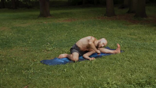 Individual practicing deep hamstring flexibility exercise on grassy surface