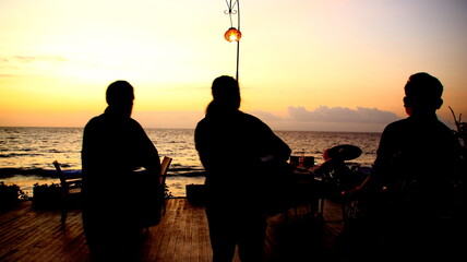 Fototapeta premium Three musicians play steel drums on a wooden pier at sunset, creating a peaceful and relaxing atmosphere with the ocean waves in the distance.