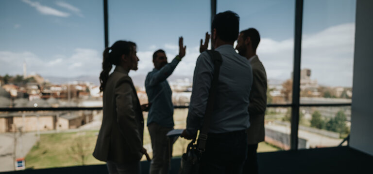 A group of coworkers in a modern office overlooks the city, sharing a high five to celebrate a milestone. The scene feels collaborative, energetic, and upbeat, highlighting teamwork.