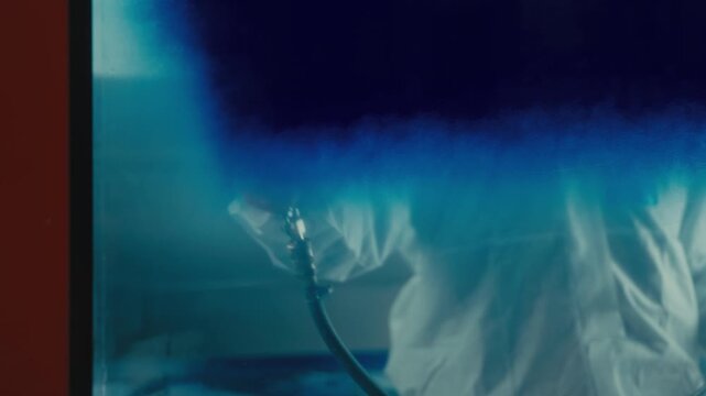 Worker Spraying Blue Paint on Glass Panel