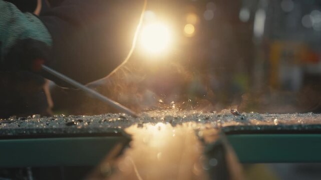 Worker Scraping Glass Debris with Screwdriver Under Intense Workshop Light