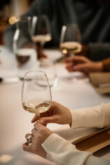 Caucasian young adult woman holding wine glass, participating in wine tasting with multiethnic group of adults, hands visible on table, engaging in sensory evaluation of wine
