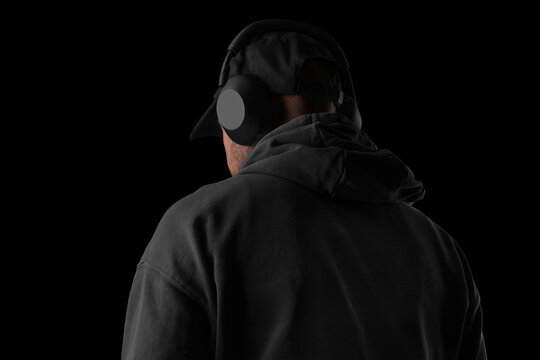 Back-view shot of a person wearing large over-ear headphones and a cap, captured in dark, dramatic lighting. Perfect for audio gear promotions, tech branding, product mockups, and lifestyle visuals.