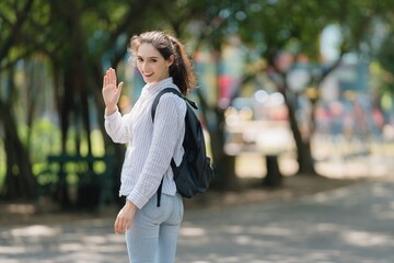 Smiling professional woman turning back and actively waving, friendly welcome, greeting, and confident communication outdoors