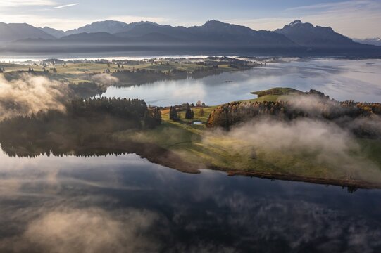 Aerial view of a lake in front of mountains in the morning light, fog, autumn, Forggensee, view of S&auml;uling and Ammergebirge, Alpine foothills, Upper Bavaria, Bavaria, Germany