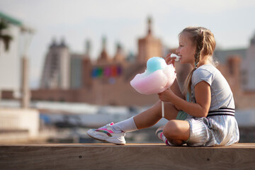 Little blonde girl with colorful braids eating vibrant cotton candy outdoors