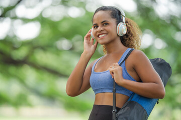 Smiling woman looking at camera with headphones and yoga mat, fitness motivation and approachable wellness guide