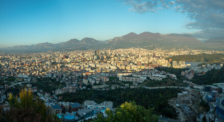 Sweeping views of Tirana's densely packed, rapidly transforming cityscape and modern towers, framed by rugged mountains under a clear sky.