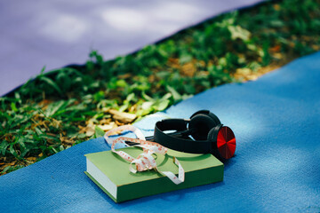 Holistic wellness tools on yoga mat: measuring tape, headphones, and book mind-body health and fitness goal tracking