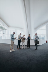 A diverse team of coworkers stands in a spacious white atrium, reviewing papers and notes. They...