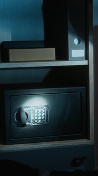 Vertical shot of anonymous robber wearing black gloves unlocking electronic safe on second try, taking money stacks and gold ingot out