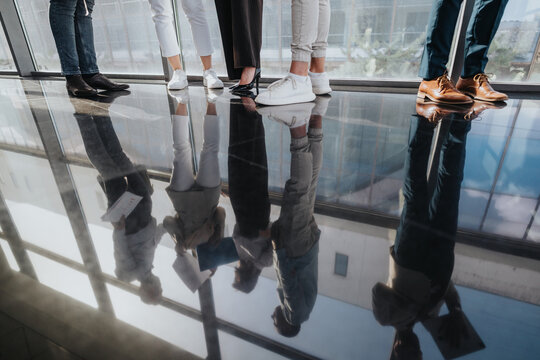 A diverse group of professionals stands in a contemporary office lobby, their reflections visible on a polished glass floor.
