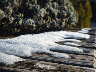 melting snow and ice crystals on wooden bench in warm sunlight
