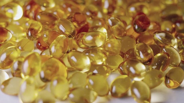 Top-down, close-up video of golden softgel capsules, like vitamin or fish oil supplements, slowly rotating on a turntable on white background showing concepts of healthcare, medicine, and nutrition.