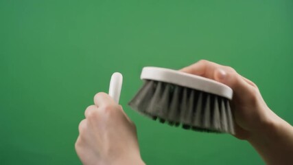 Hands holding and demonstrating a cleaning brush against a green screen background.