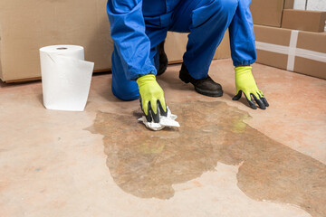 Male worker cleaning-up a slip hazard on the floor of an industrial plant with white paper.