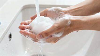 Fototapeta premium Man washing hands with soapy foam under running water for personal hygiene routine