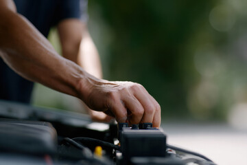 Hand adjusting fuse box settings in car engine compartment with blurred natural background