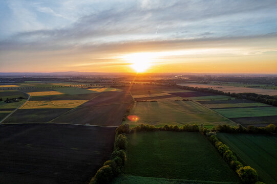 Aerial view of the sun setting over patchwork fields, casting long shadows and warm hues across the landscape, Mannheim, Baden-Wurttemberg, Germany.