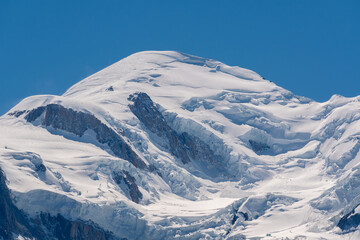 A detailed close-up of the massive, snow-covered summit of Mont Blanc, showing deep crevasses and ice formations under a clear, intense blue sky.