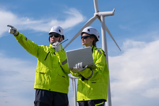 Two engineers working on a wind farm site during a sunny day while assessing project progress and technology use